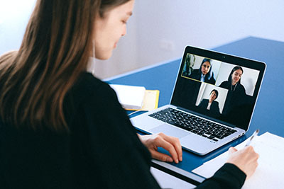 A female-presenting person has a video conference on a laptop. Three other people are on her laptop screen.