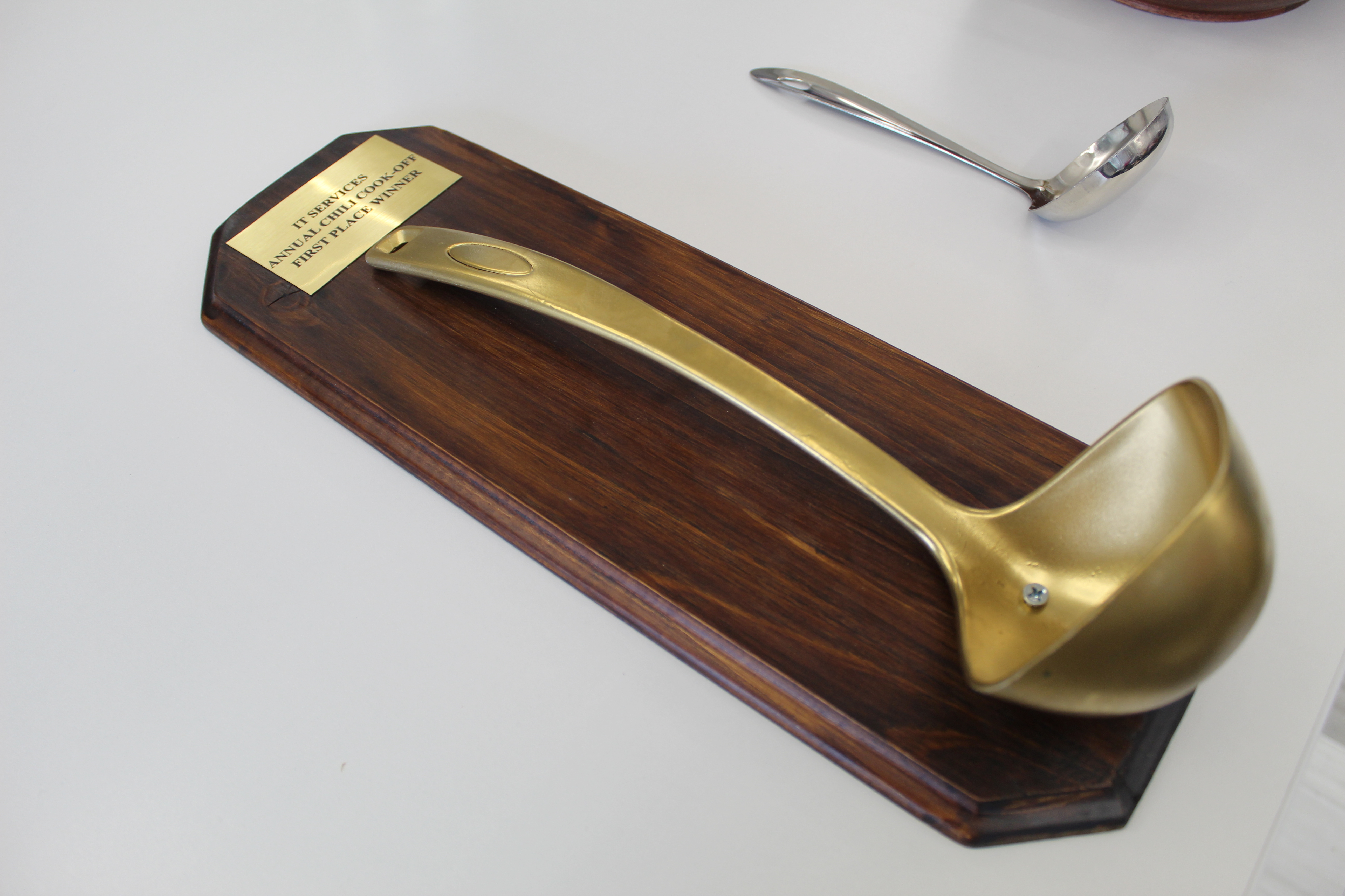 A golden ladle on a wooden plaque. The plaque says IT Services Annual Chili Competition First Place Winner