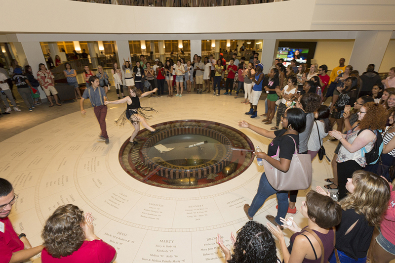 Swing dancers dance on the seal in the Armstrong Student Center while an encircling crown watches