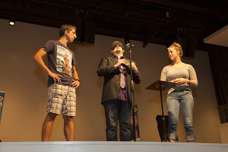 A performer and two students stand on the stage in Wilks Theater