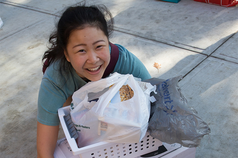 A student smiles as she bends down to lift a pile of boxes