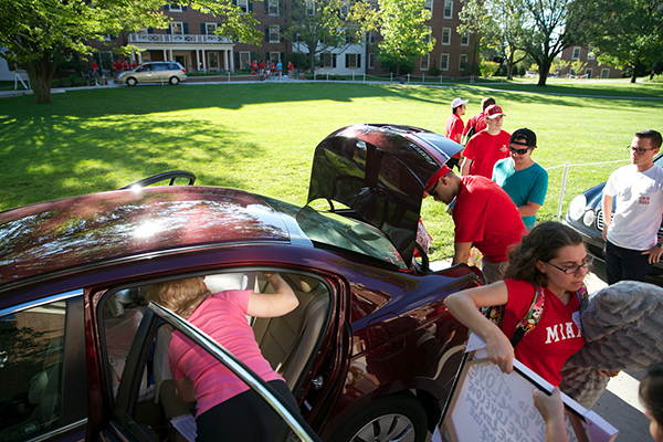 Volunteers line up to help unload a car with all doors and the trunk open