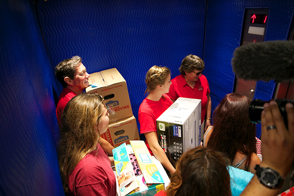 President and Mrs. Hodge, along with student volunteers, stand in a blue elevator holding a variety of boxes