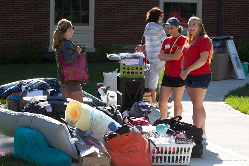 Two volunteer helpers wait by a pile of stuff that is waiting to be moved in to a dorm room