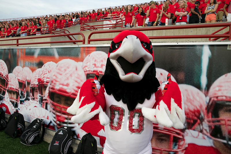 Swoop stands on the Foodball field in front of the stands, which are filled with students