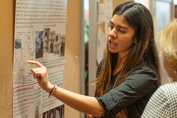 A graduate student points to a portion of her research poster as a visitor looks on