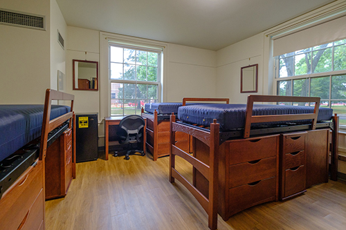 Room in resident hall with three lofted beds and wood floors