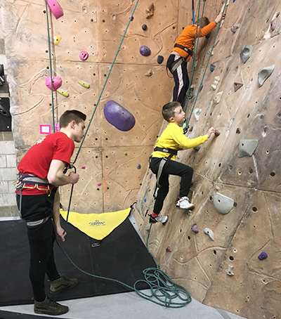 Two children on the climbing wall and a Miami student helping one child