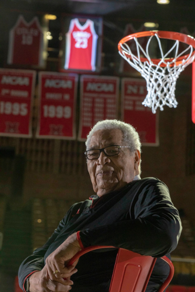Wayne Embry sits on the Millett Hall court with his retired No. 23 jersey spotlighted in the background.