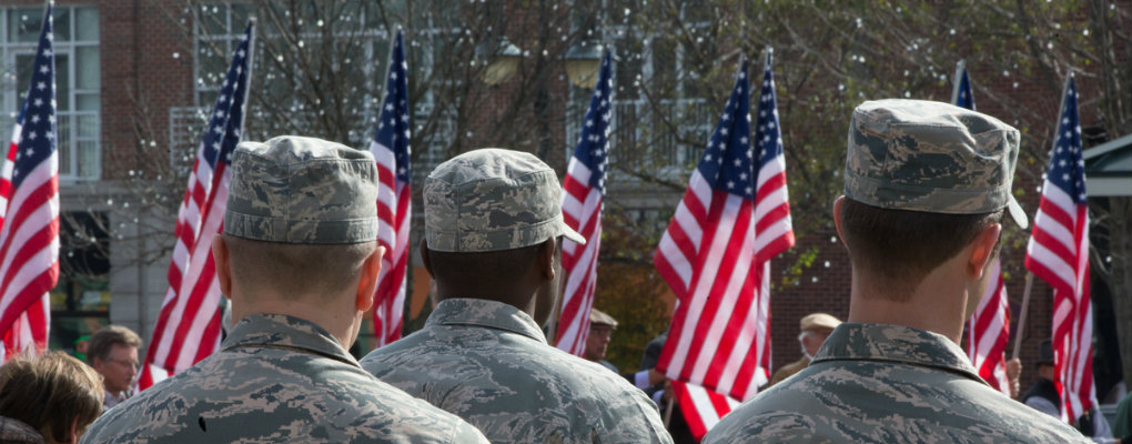 Uniformed members of the military face a bank of American flags in a Veterans Day event