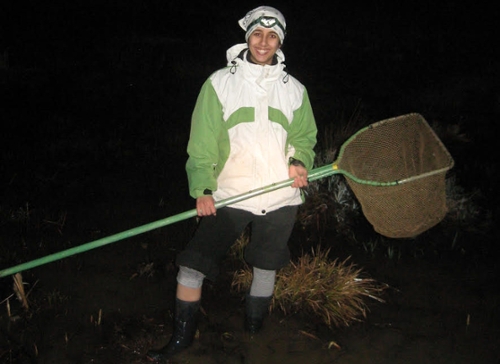 Clara do Amaral, in jacket and cap, holds a long-handled net as she works in a dark field