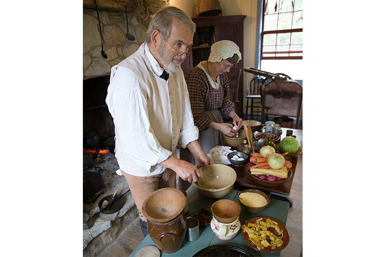 Actors portraying people from history as they prepare food for cooking in a stone fireplace