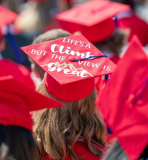student at commencement wearing acustomized mortar board that says "Life's a climb, but the view is great"