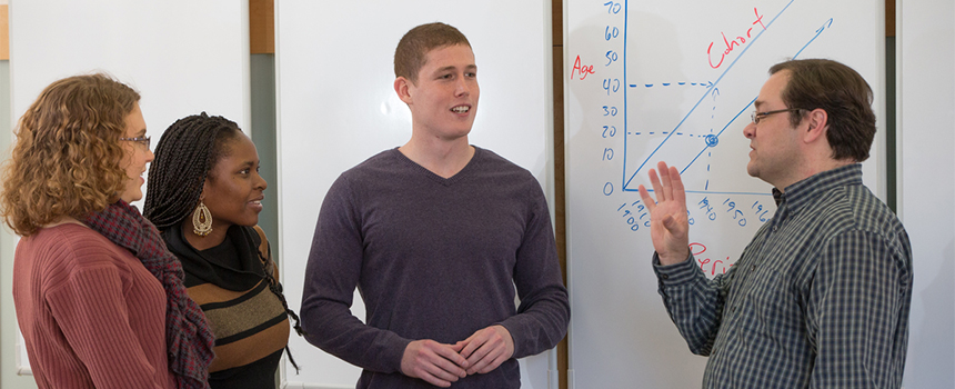 A professor and students converse in front of a whiteboard showing data