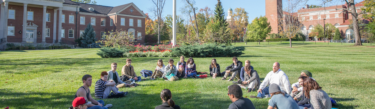 A professor and students hold class on the lawn of Roudebush Hall