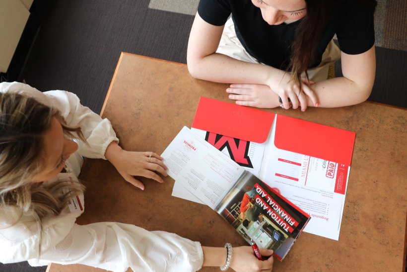 Two students looking through a red folder filled with admission information
