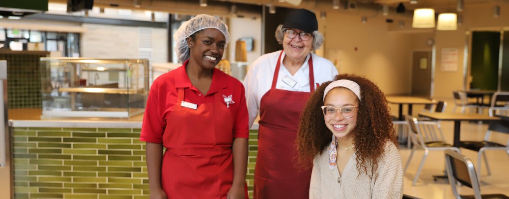  Two dining employees smiling for a photo with a student.
