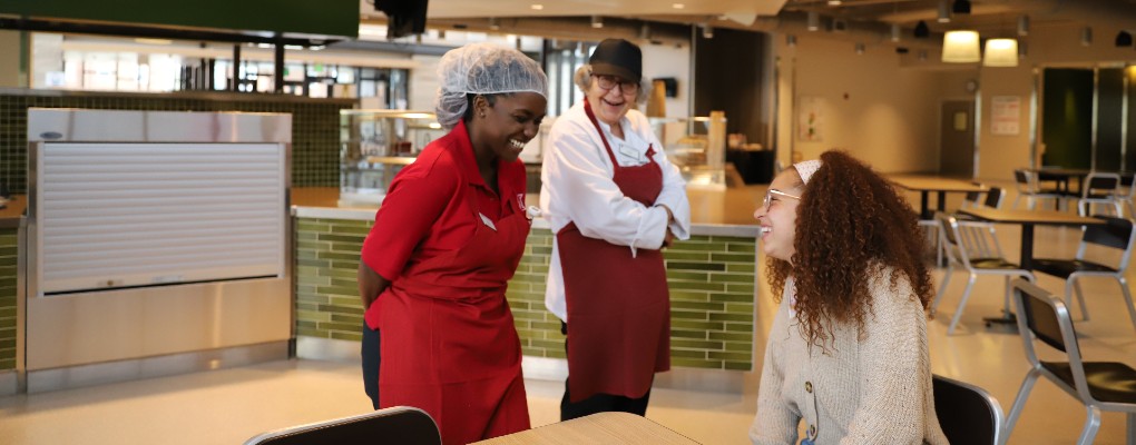  Two dining employees laughing with a student.
