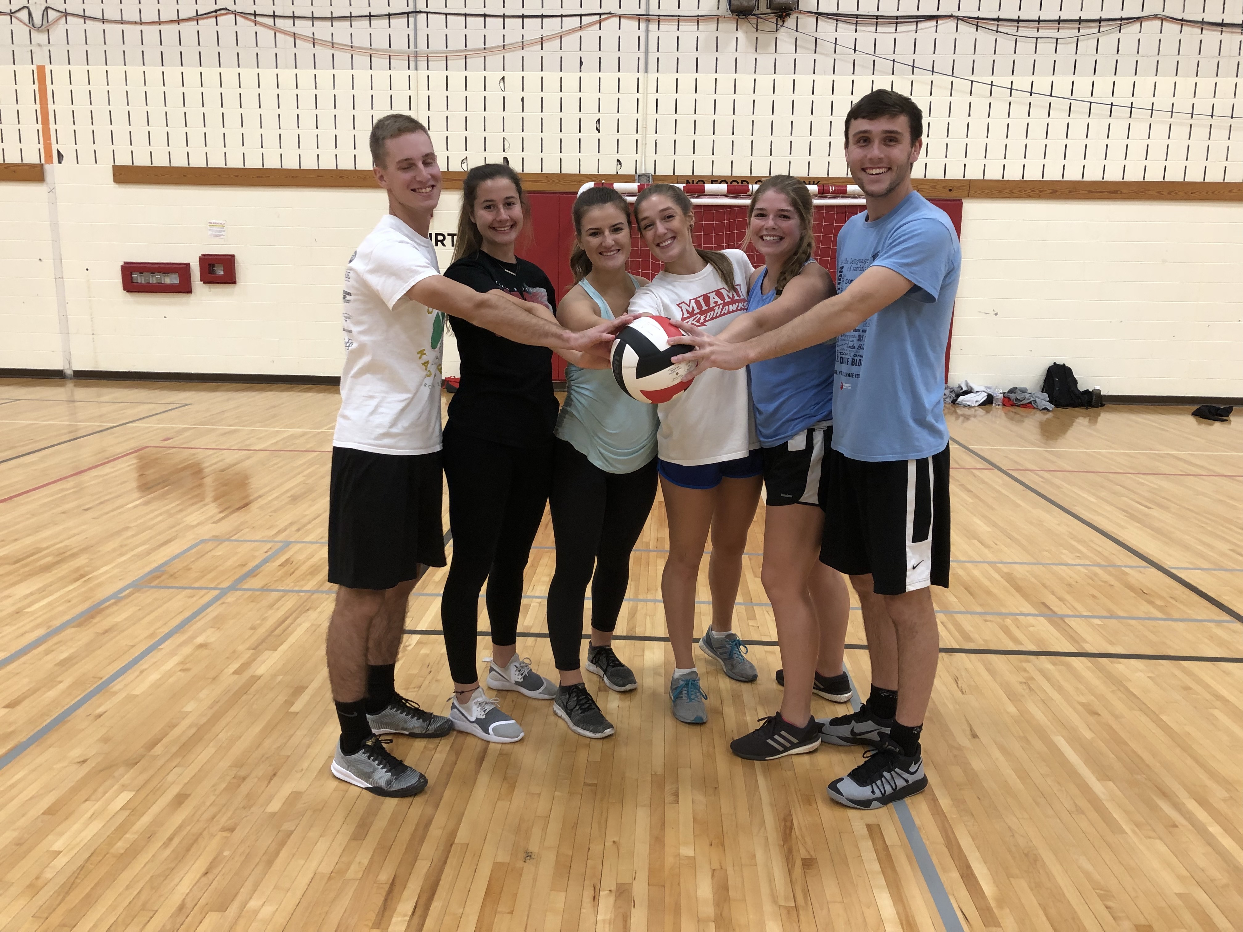 Indoor volleyball runner up team poses together with one hand of each player touching the game-used volleyball.