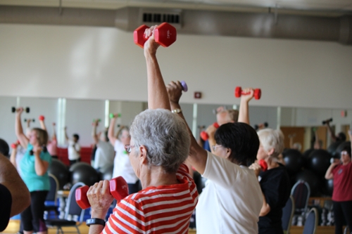 SilverSneakers members stretch their arms up while using hand weights during a program.