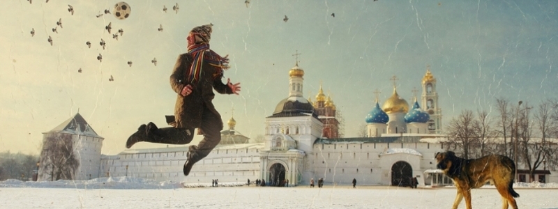 Russian artwork showing a child playing soccer with his dog in the snow, near a city with domed towers. 