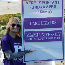 A student poses near a sign that highlights Miami Gerontology achievement at Alzheimers Walk