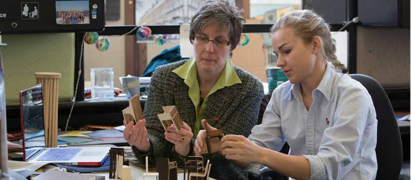Professor and student converse as they hold and examine small models of furniture