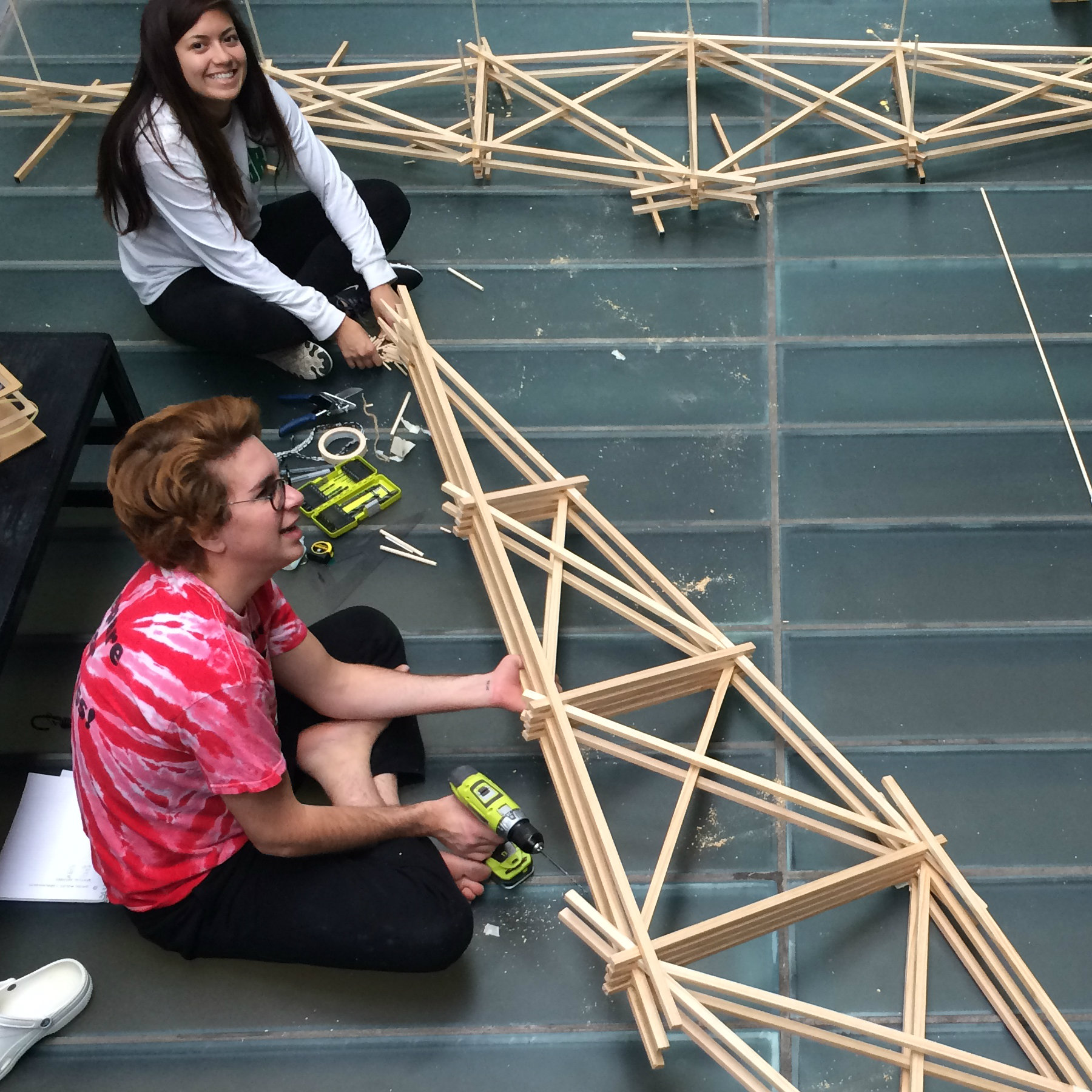 students sitting on floor of atrium with large bridge models