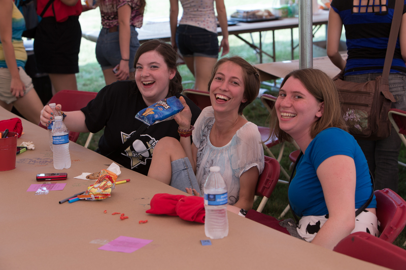  Three smiling students seated under the tent at the Lawn Party