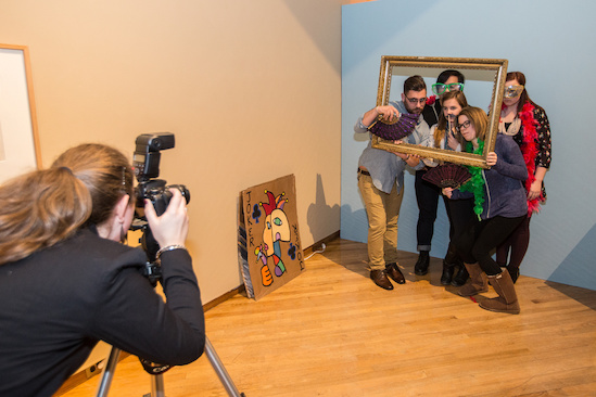 A photographer leans in for a photo of students posing behind a large rectangular open picture frame