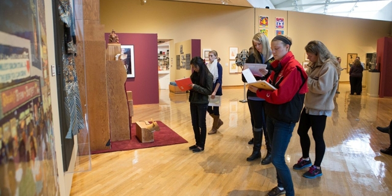  A wide view of students gathered in small groups as they take notes on artwork in the gallery