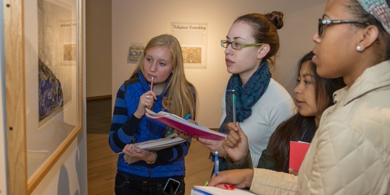  Students holding notepads peer intently at a picture in the gallery