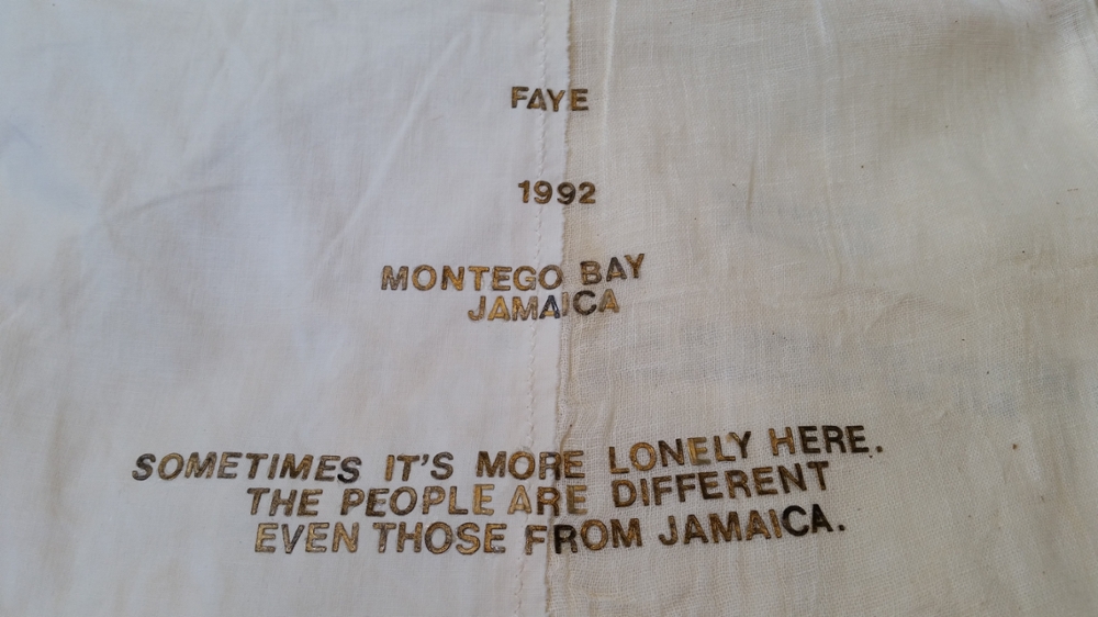 A textile from the exhibit. Words: Faye 1992. Montego Bay Jamaica. Sometimes it's more lonely here. The people are different even from those from Jamaica'