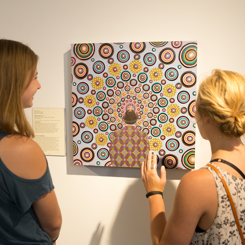 2 women examine a work of art on the wall