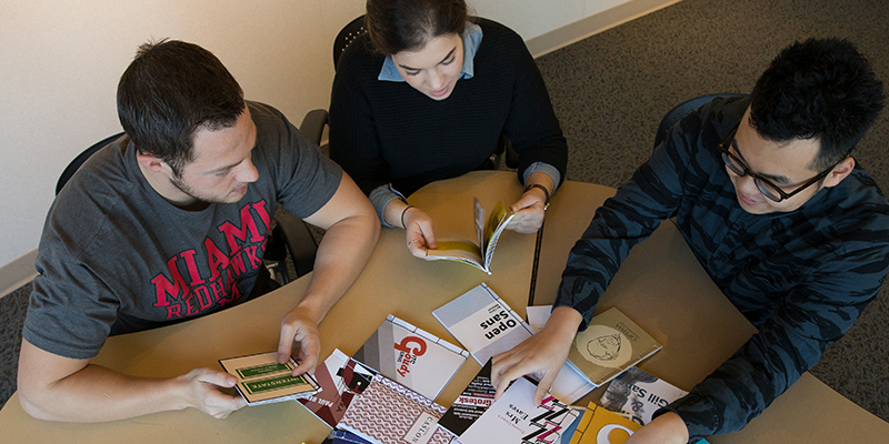  An overhead view of students working at a table with print materials during ART 251 typography class