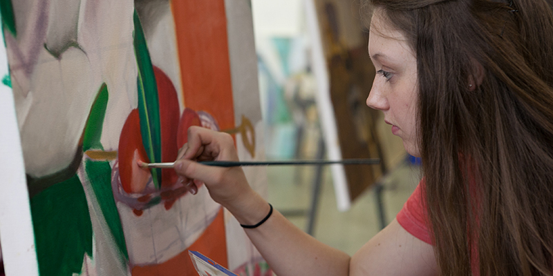 2D studio student focuses as she paints a canvas 