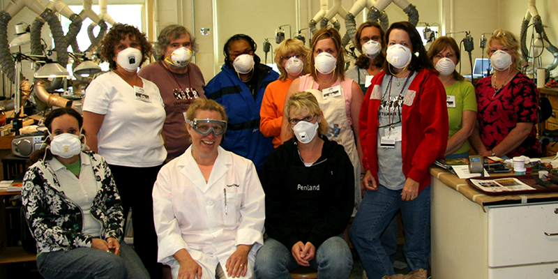 Students in an enameling studio wear face masks as they pose for a group photo