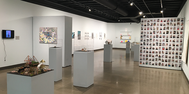 A view of Hiestand Galleries showing multimedia exhibits and a wall covered with snapshot sized photos
