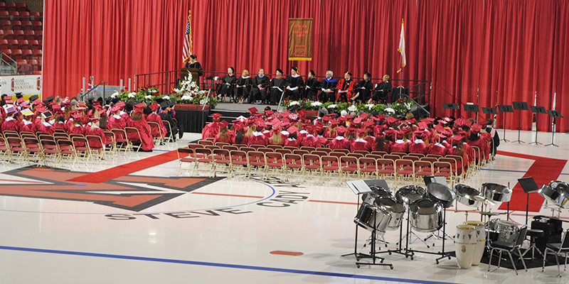 CCA graduates in red caps and gowns listen to a speaker at the CCA Recognition Ceremony at Goggin Ice Arena