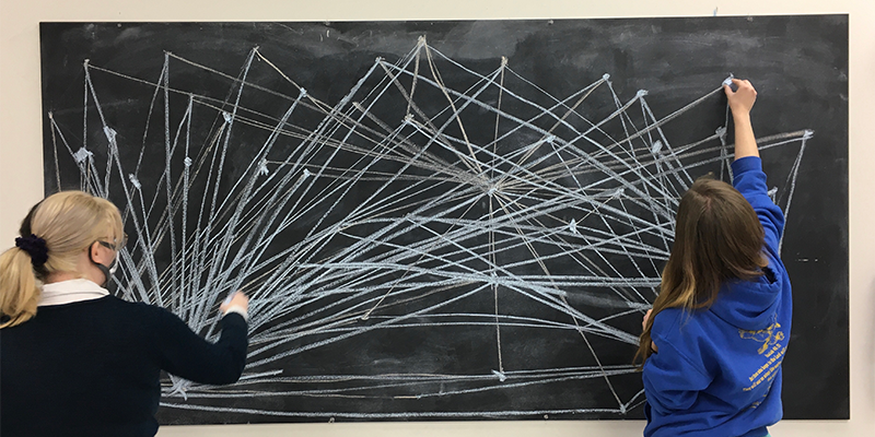 at a chalkboard, two people create math art