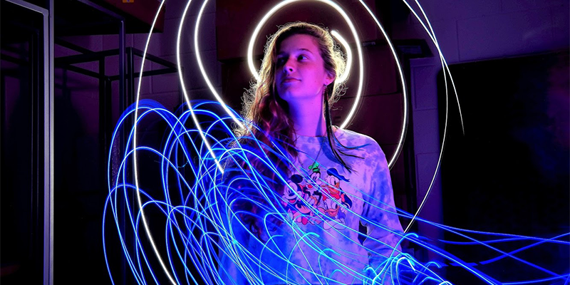 a woman stands amid swirling light paths in a darkened room