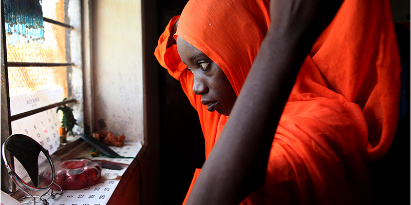  a young woman garbed in orange looks out a window