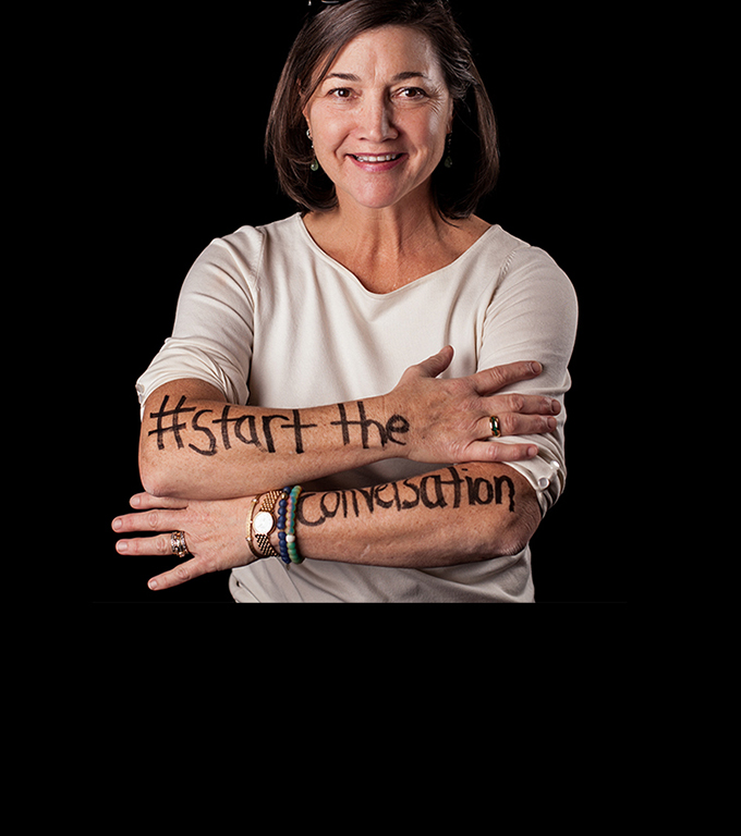 A woman participating in Dear World crosses her arms to reveal writing hashtag Start the conversation
