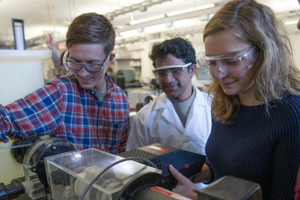 Students wearing lab goggles work with a machine