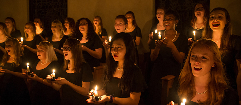 Singers hold lit candles and sing in muted lighting during the annual Ceremony of Carols performance by Choraliers (2016)