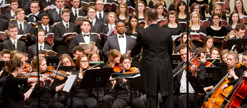 A mixed chorus sings, accompanied by the Miami symphony orchestra onstage at Hall Auditorium