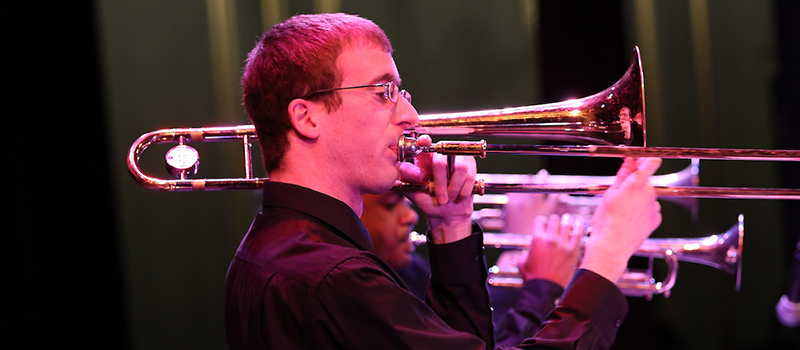 A trombone player is seen from the side as he performs at the Jazz Ensemble concert 