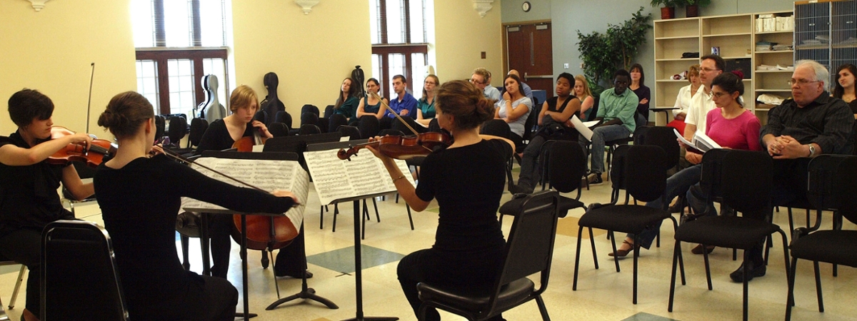 During a coaching session, a string quartet performs in a classroom with onlookers