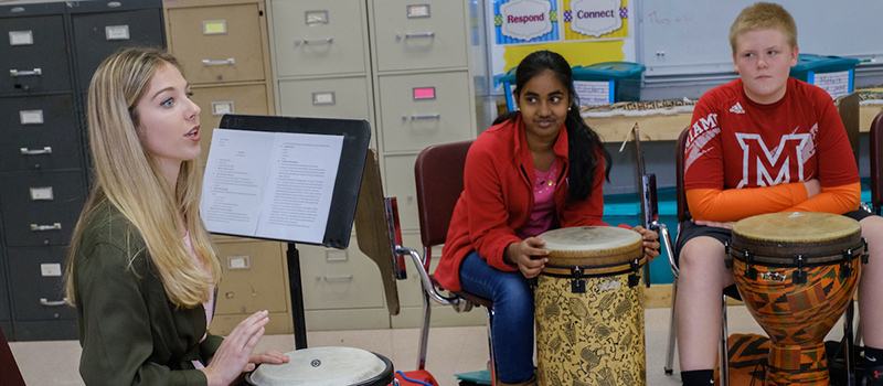 A student teacher leads her students in a drumming lesson