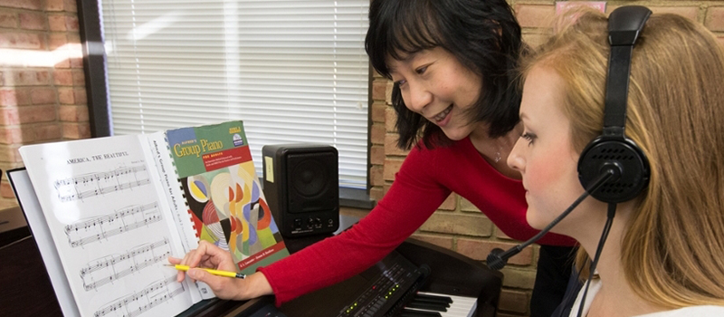 Dr. Tan works with a student wearing headphones who is participating in group piano class